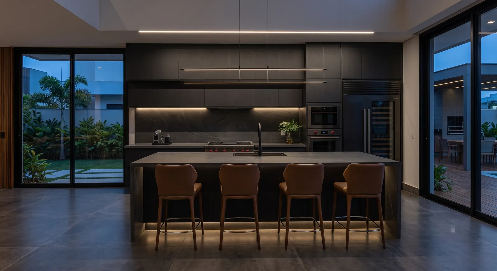 Cozinha em tons de carvão com iluminação linear, ilha em pedra e banquetas em couro caramelo